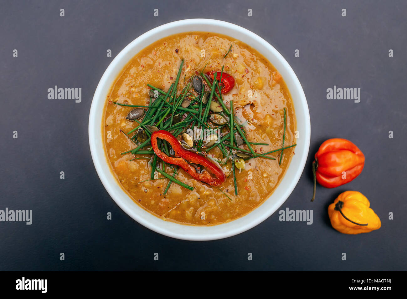 White bowl of a healthy vegetarian pea soup with pumpkin seeds, chives and spicy chilli. Orange color, black background, dark food photography Stock Photo
