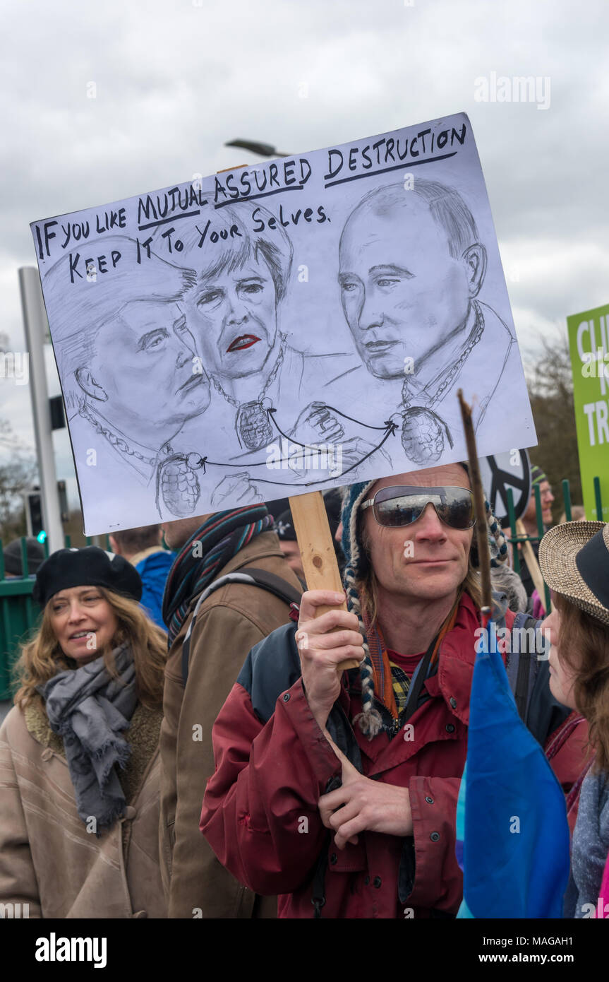 Aldermaston, UK. 1st Apr, 2018. A protest holds a poster showing Donald Trump, Theresa May and Vladmir PUtin at the CND celebration of the 60th anniversary of the first Aldermaston march which mobilised thousands against the Bomb and shaped radical protest for generations. Their protest outside the Atomic Weapons Establishment included a giant, iconic peace symbol, speeches, including by some of those on the original march, singing and drumming and celebrated the UN treaty banning nuclear weapons. Credit: Peter Marshall/Alamy Live News Stock Photo