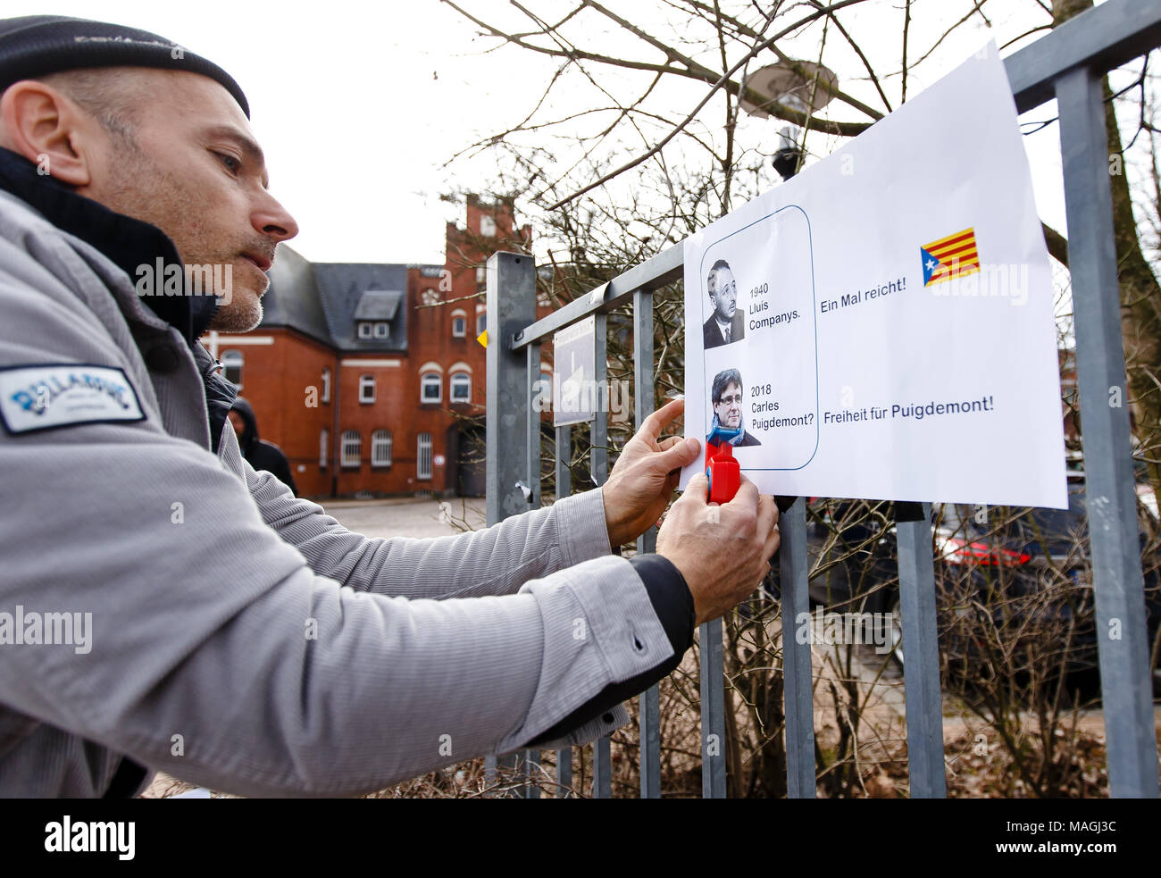 02 April 2018, Germany, Neumuenster:The German-Catalan Jorge Ponsetti hangs up a paper with pictures of Lluis Companys and Carles Puigdemont outside the Neumuenster prison. Companys was on the run as President of the Catalan Republic in 1939 in France, was arrested by the Gestapo and extradited to Spain in 1940. The former President of Catalonia Puigdemont is held in custody since his arrest on 25 March 2018 at the Neumuenster prison. Photo: Frank Molter/dpa Stock Photo
