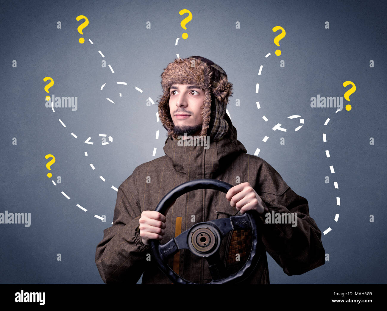 Young man holding black steering wheel with question marks around him
