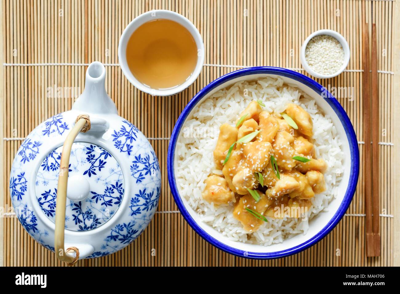 Chinese orange chicken with rice, china teapot and cup of green tea on bamboo background. Top view. Traditional chinese cuisine Stock Photo
