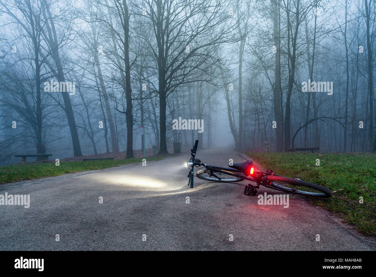 A bycicle left alone in the park street at nighttime with the lights on  The scene suggests a kidnap or a crime Stock Photo