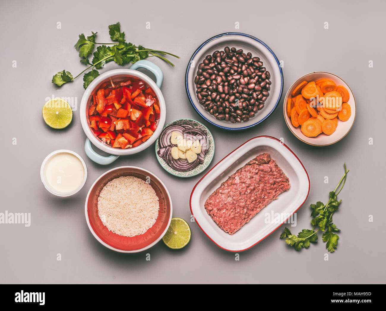 Flat lay of bowls with cooking ingredients for balanced one pan meal with beans, minced meat, rice and various cut vegetables on gray background, top  Stock Photo