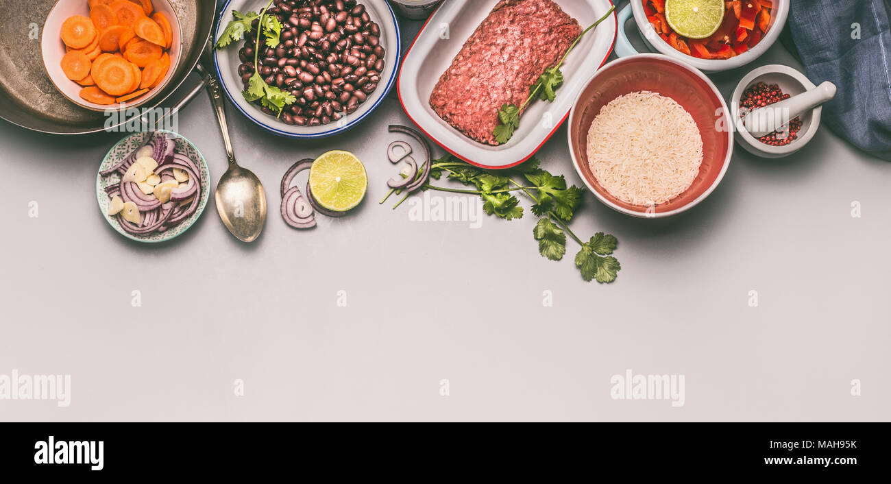 Bowls with cooking ingredients for balanced one pan meal with beans, minced meat, rice and various cut vegetables on gray background, top view Stock Photo