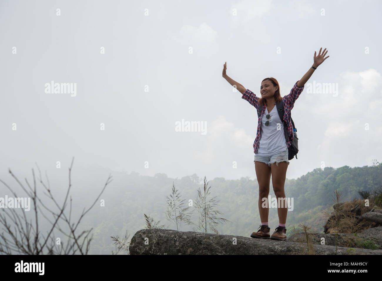 Hiker with backpack standing on top of a mountain with raised hands and ...