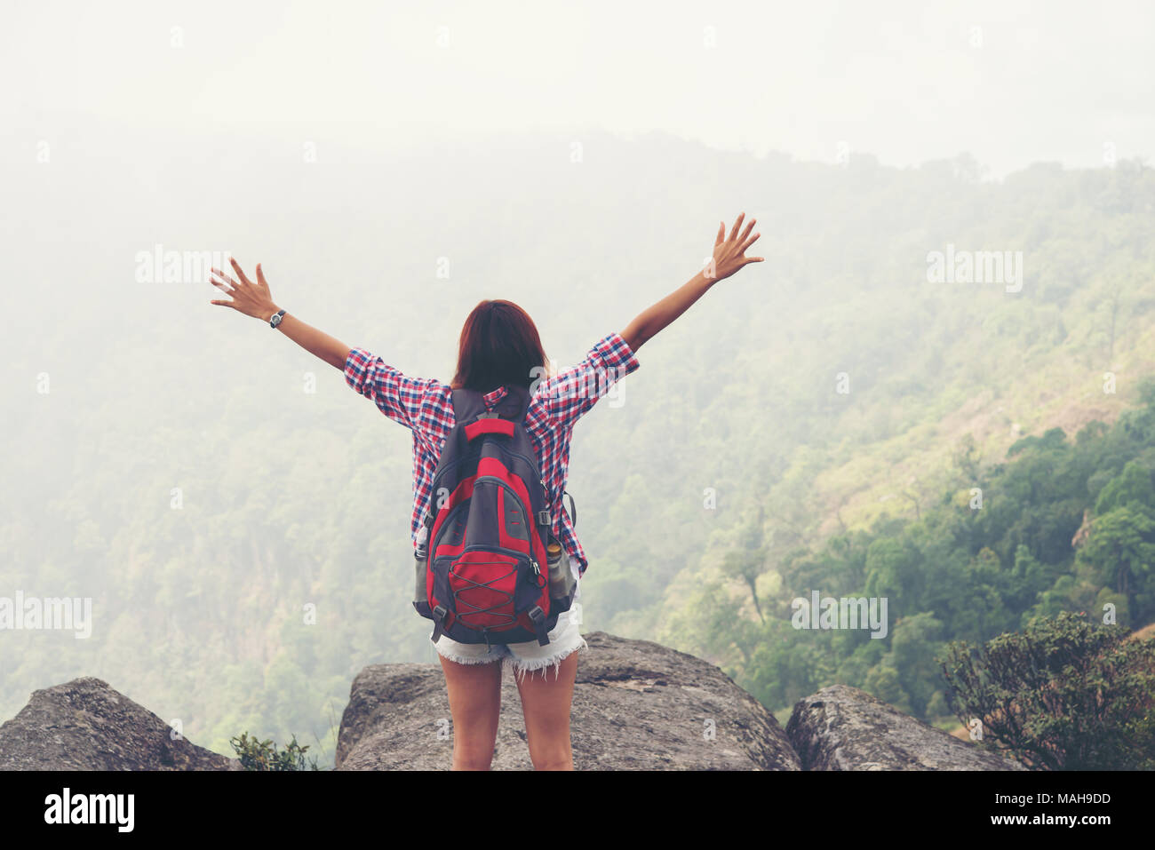 Hiker with backpack standing on top of a mountain with raised hands and ...