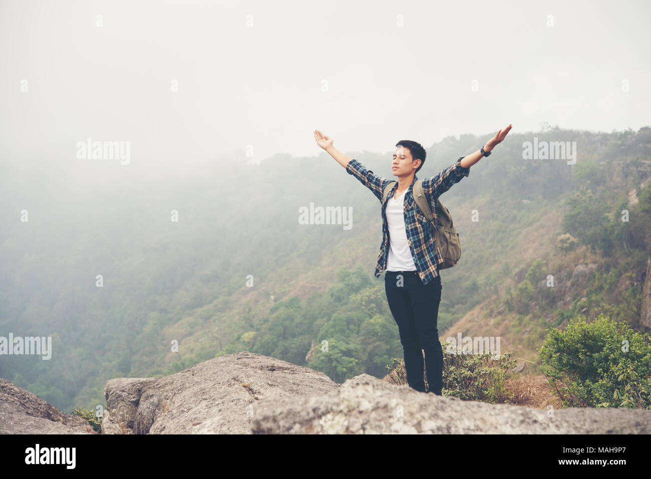 Hiker with backpack standing on top of a mountain with raised hands ...