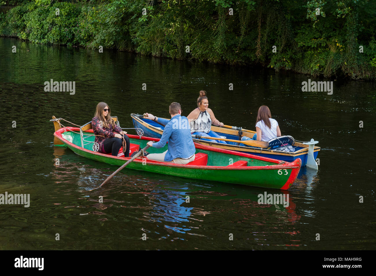 4 people boating in pairs, relaxing & having fun in 2 rowing boats side by side & about to collide - River Nidd in summer, Knaresborough, England, UK. Stock Photo