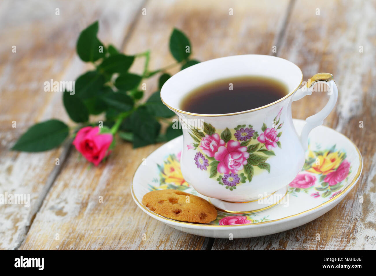 Tea in vintage porcelain cup, crunchy cookie and pink wild rose on rustic wooden surface Stock Photo