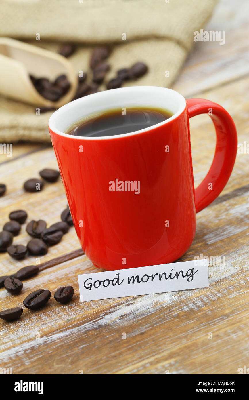 Good morning card with red mug of coffee and scattered coffee beans on rustic wooden surface Stock Photo