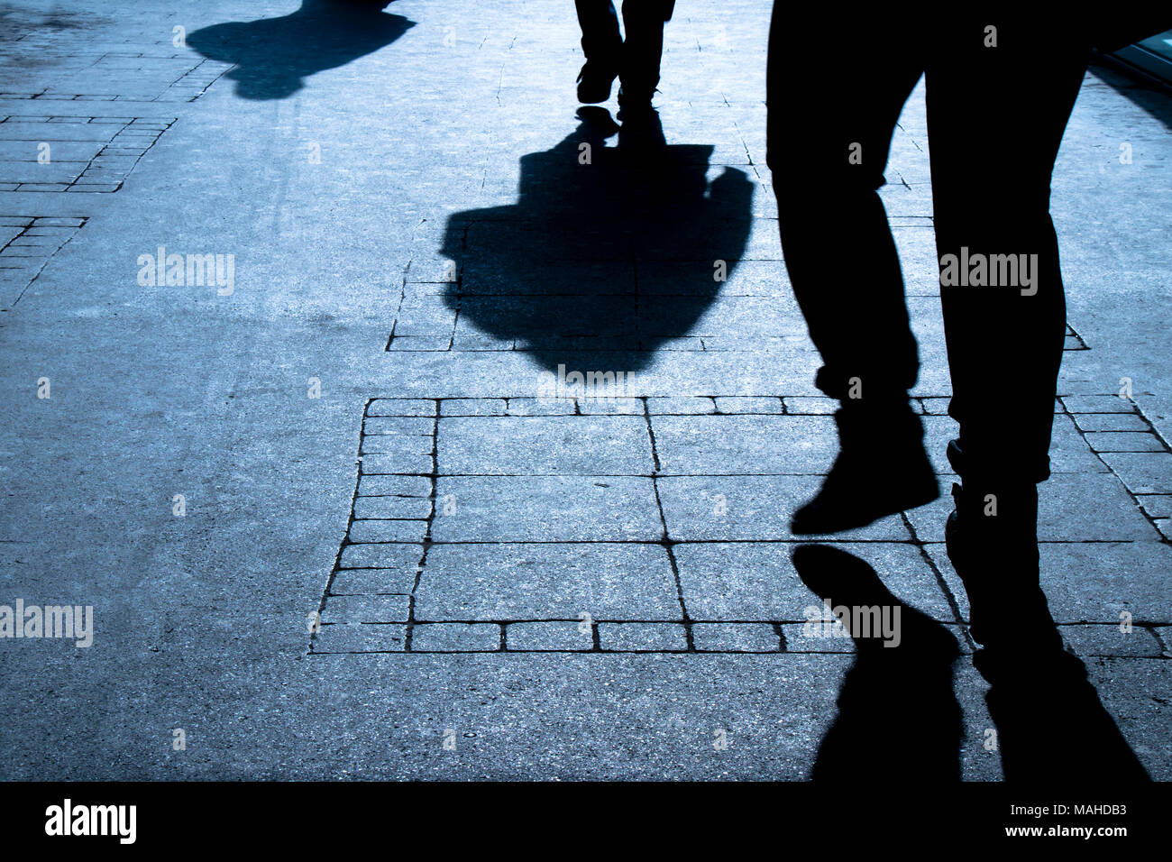 Silhouette shadows of three people walking alone on city street in the night Stock Photo
