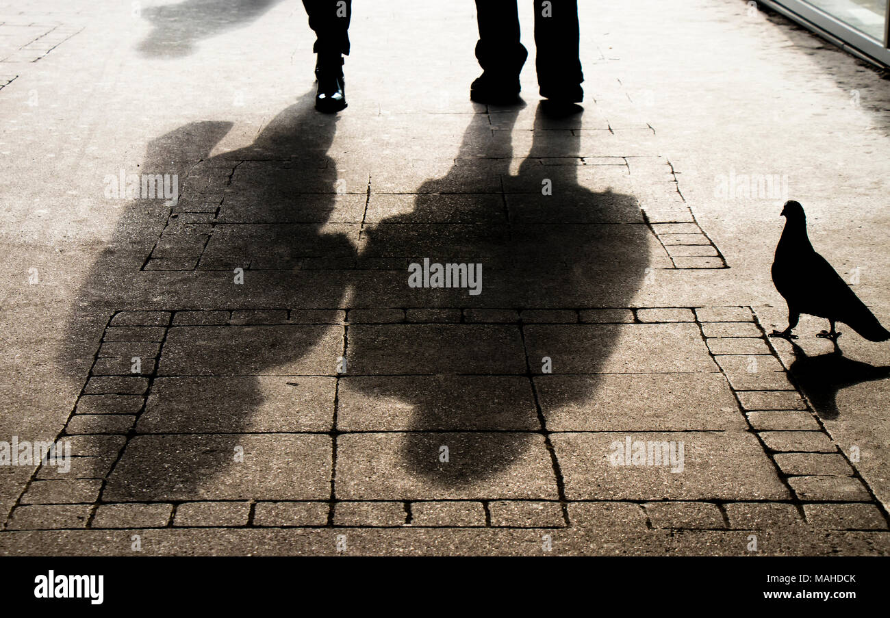 Silhouette shadow of a woman , a man and a pigeon on city sidewalk in sepia black and white Stock Photo