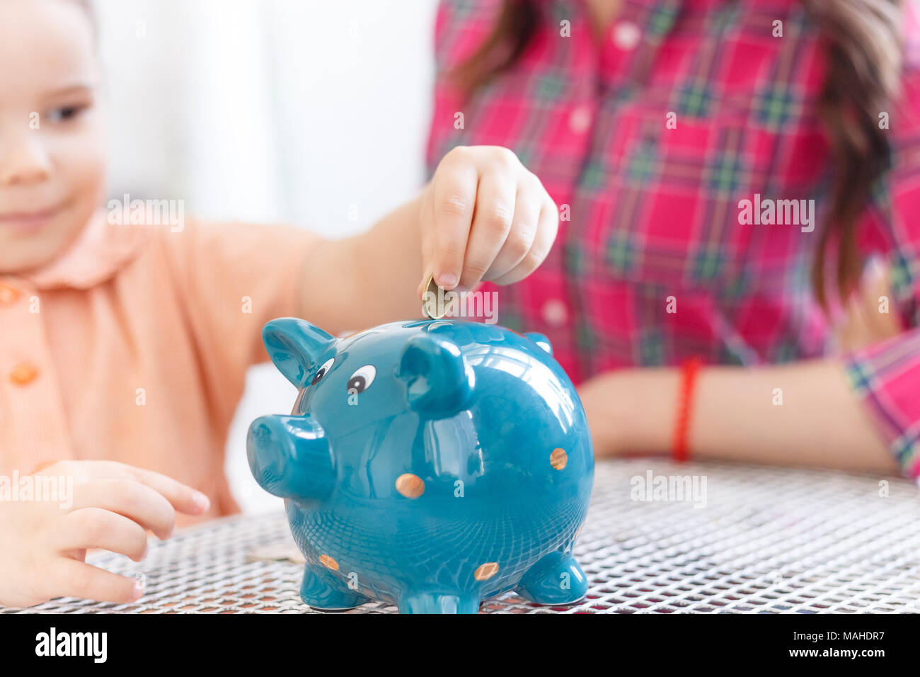 Mom teaches a little daughter to collect money in a piggy bank Stock ...