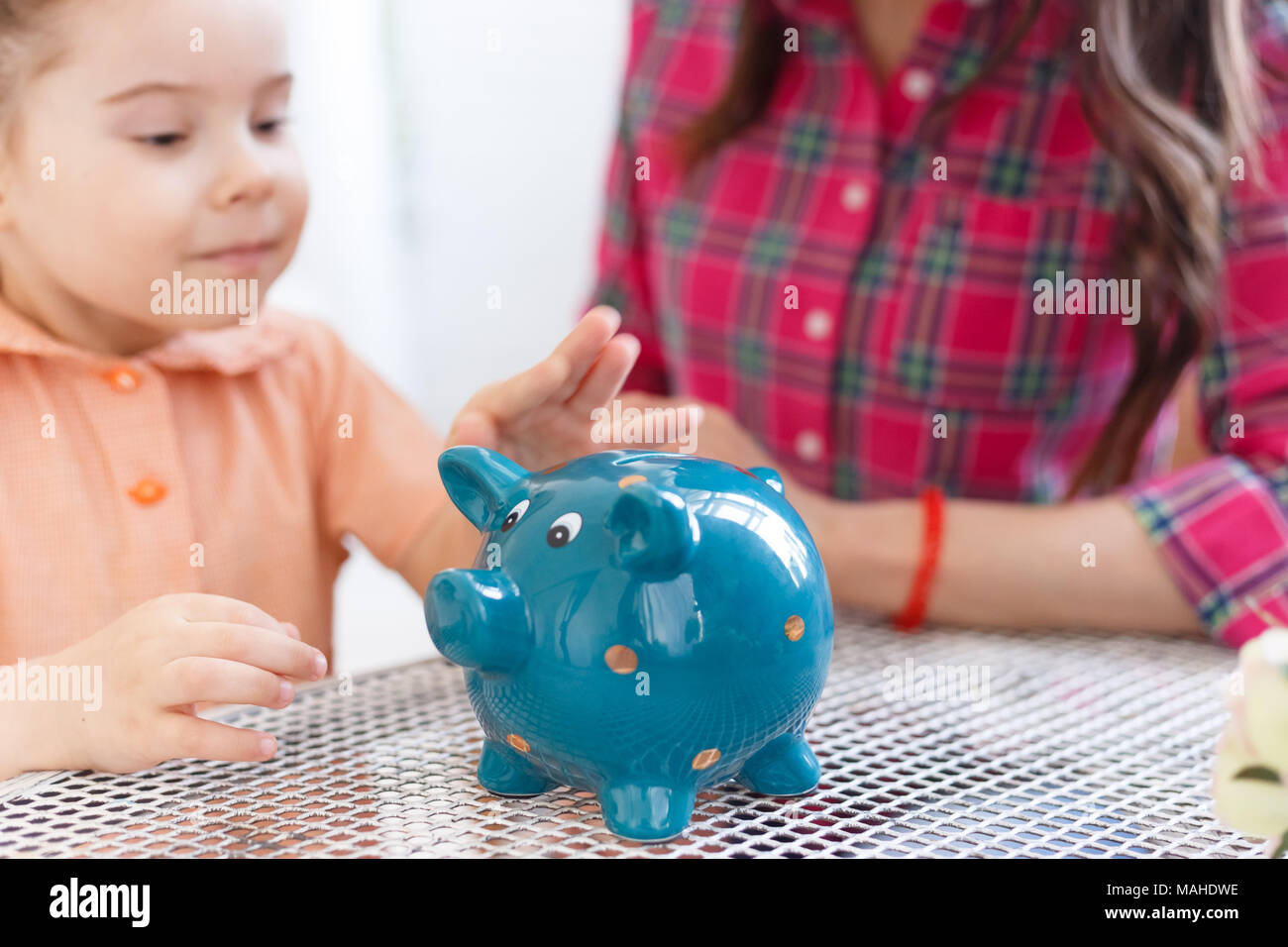 Mom teaches a little daughter to collect money in a piggy bank Stock ...