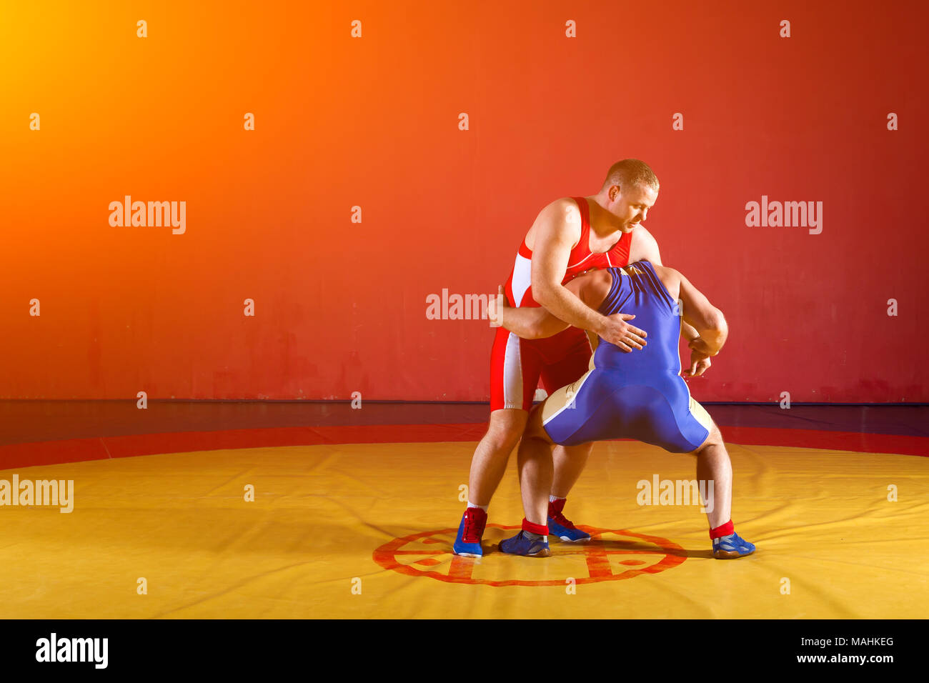 Two greco-roman  wrestlers in red and blue uniform making a   hip throw  on a yellow wrestling carpet in the gym Stock Photo