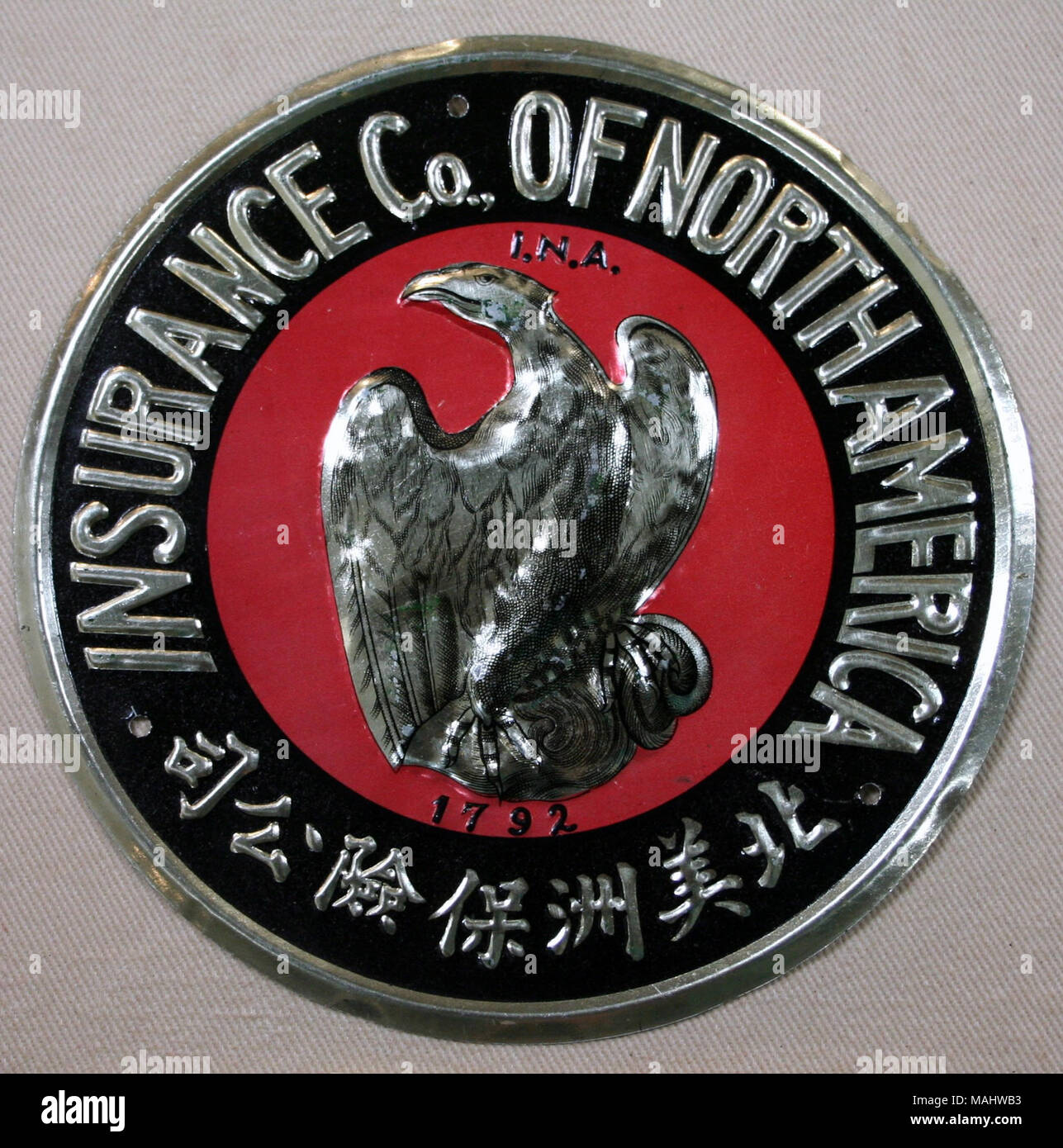Pressed tin fire mark for Insurance Company of North America in Philadelphia, Pennsylvania shows raised gold eagle on red center with company name and foreign characters around border Title: Fire mark for Insurance Company of North America in Philadelphia, Pennsylvania  . after 1920. Stock Photo