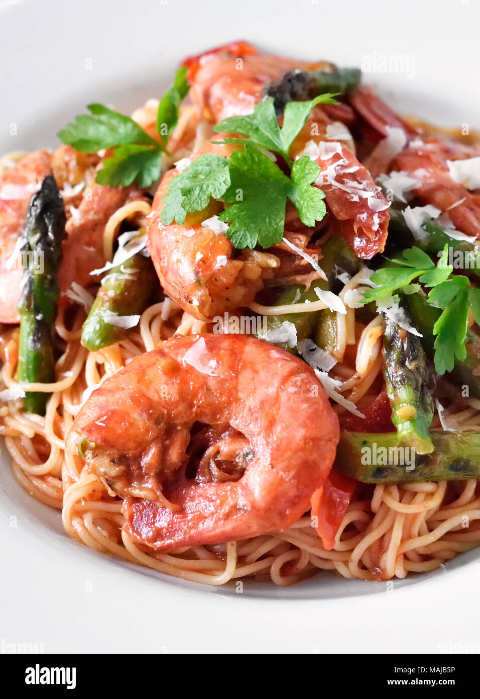 Spaghetti frutti di mare or pasta dish with shrimps and green asparagus and parsley garnish. White plate on a wooden table, healthy eating scene. Stock Photo