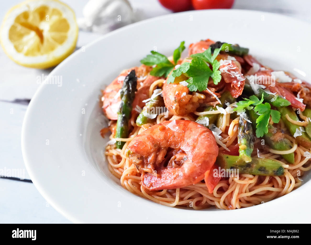 Spaghetti frutti di mare or pasta dish with shrimps and green asparagus and parsley garnish. White plate on a wooden table, healthy eating scene. Stock Photo