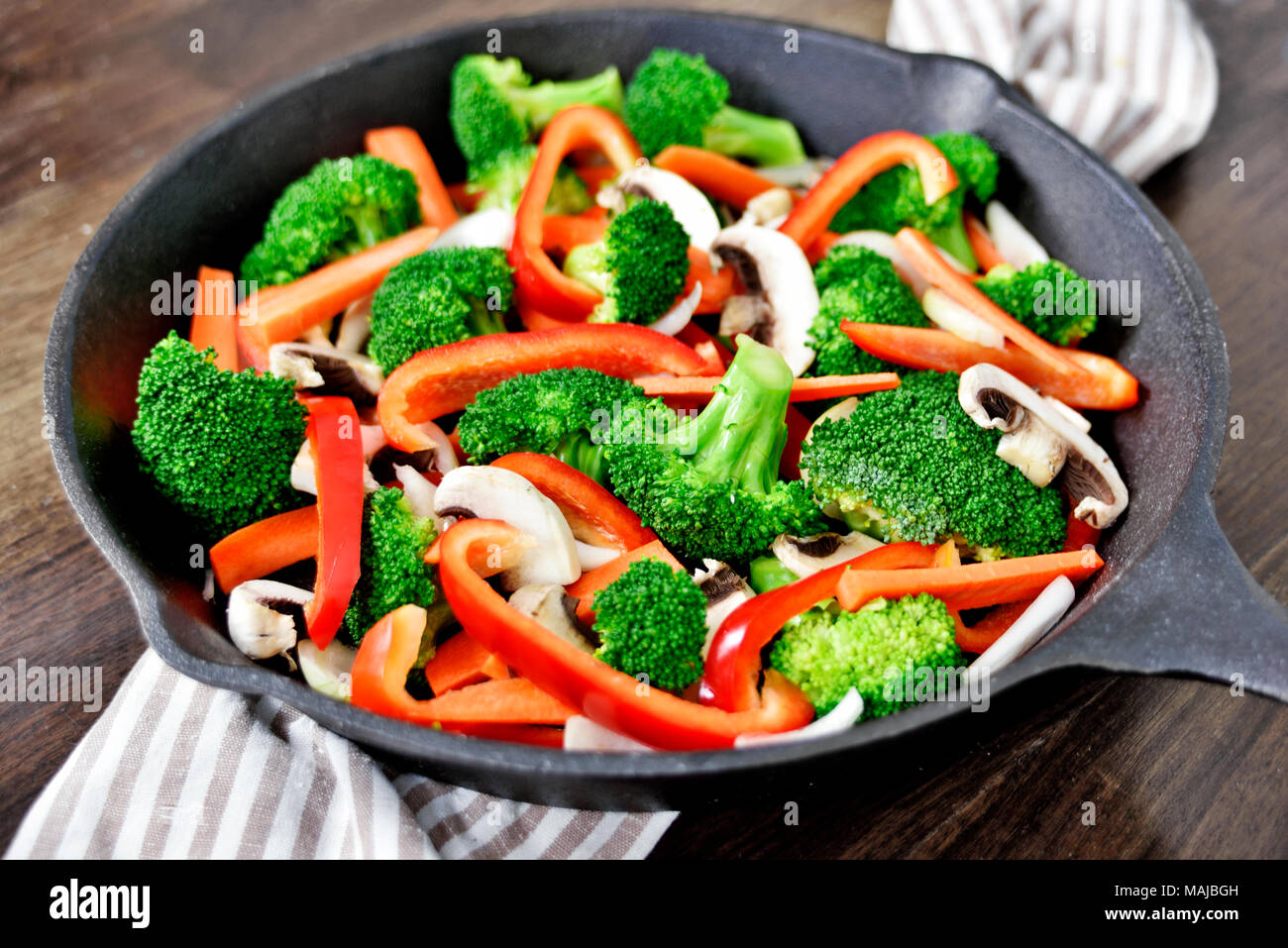 Healthy eating scene with vegetables in an iron pan or cooking pan. Broccoli, red bell pepper, carrots and white mushrooms. Stock Photo
