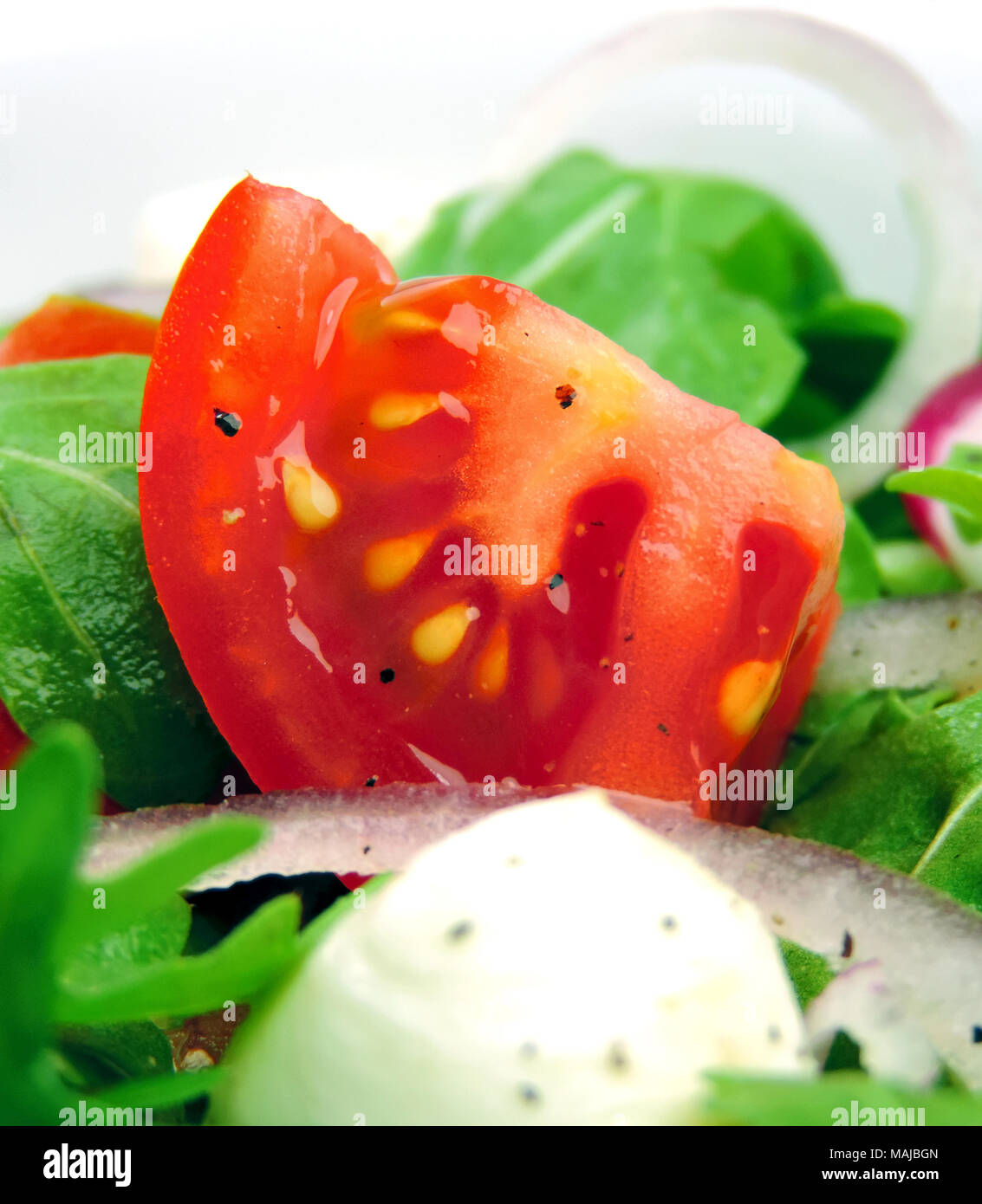Gourmet salad or fresh Caprese salad with tomatoes, red onions, rocket and mozzarella cheese on a white plate. Close-up shot of fresh salad. Stock Photo