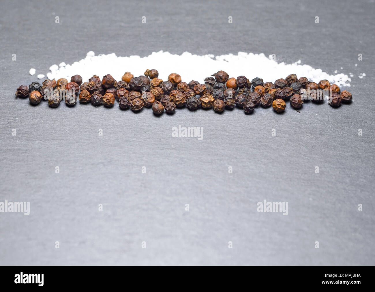 Black peppercorns and sea salt on a slate plate or black background. Spices or cooking ingredients on a rock background. Stock Photo