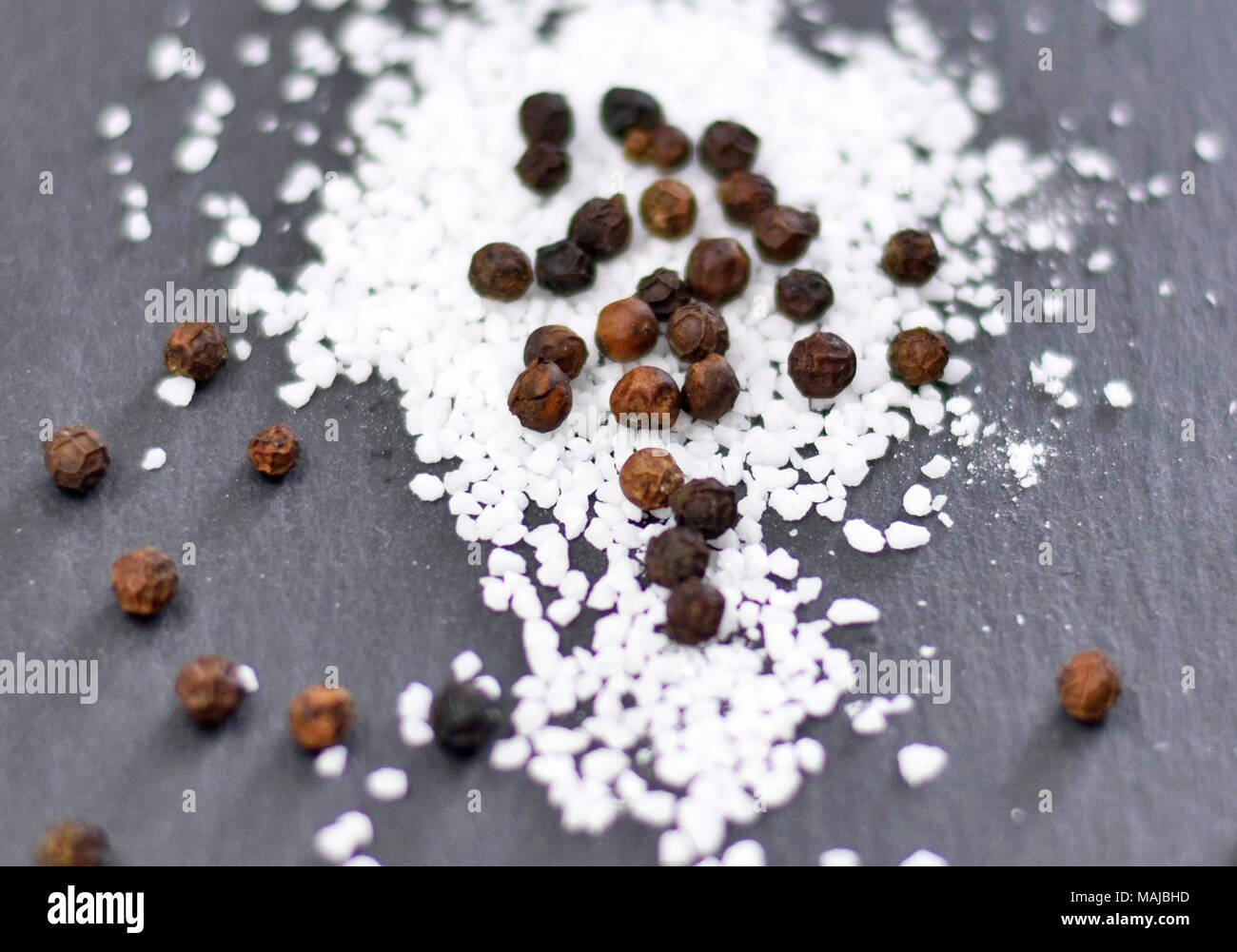Black peppercorns and sea salt on a slate plate or black background. Spices or cooking ingredients on a rock background. Stock Photo