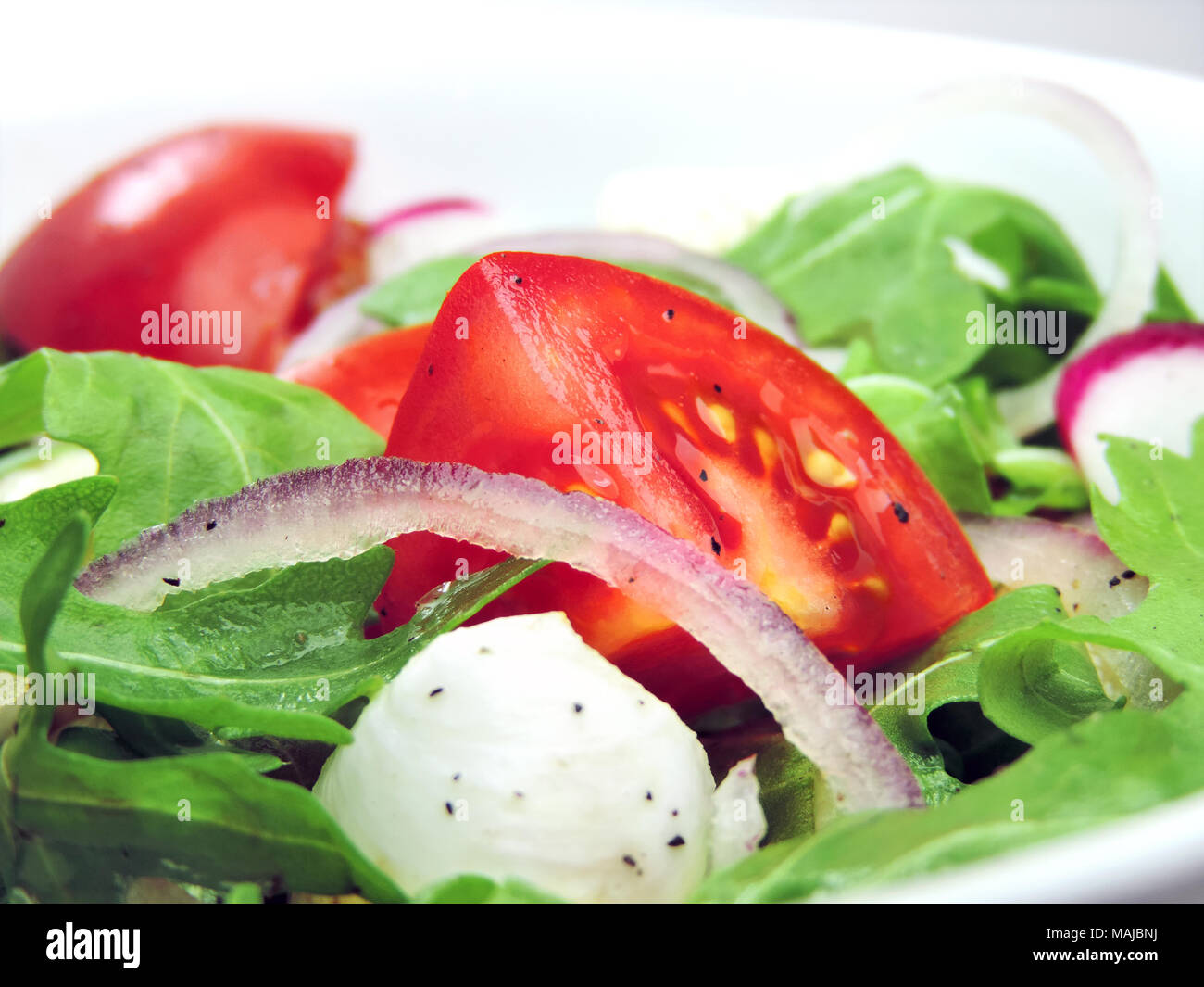 Gourmet salad or fresh Caprese salad with tomatoes, red onions, rocket and mozzarella cheese on a white plate. Close-up shot of fresh salad. Stock Photo