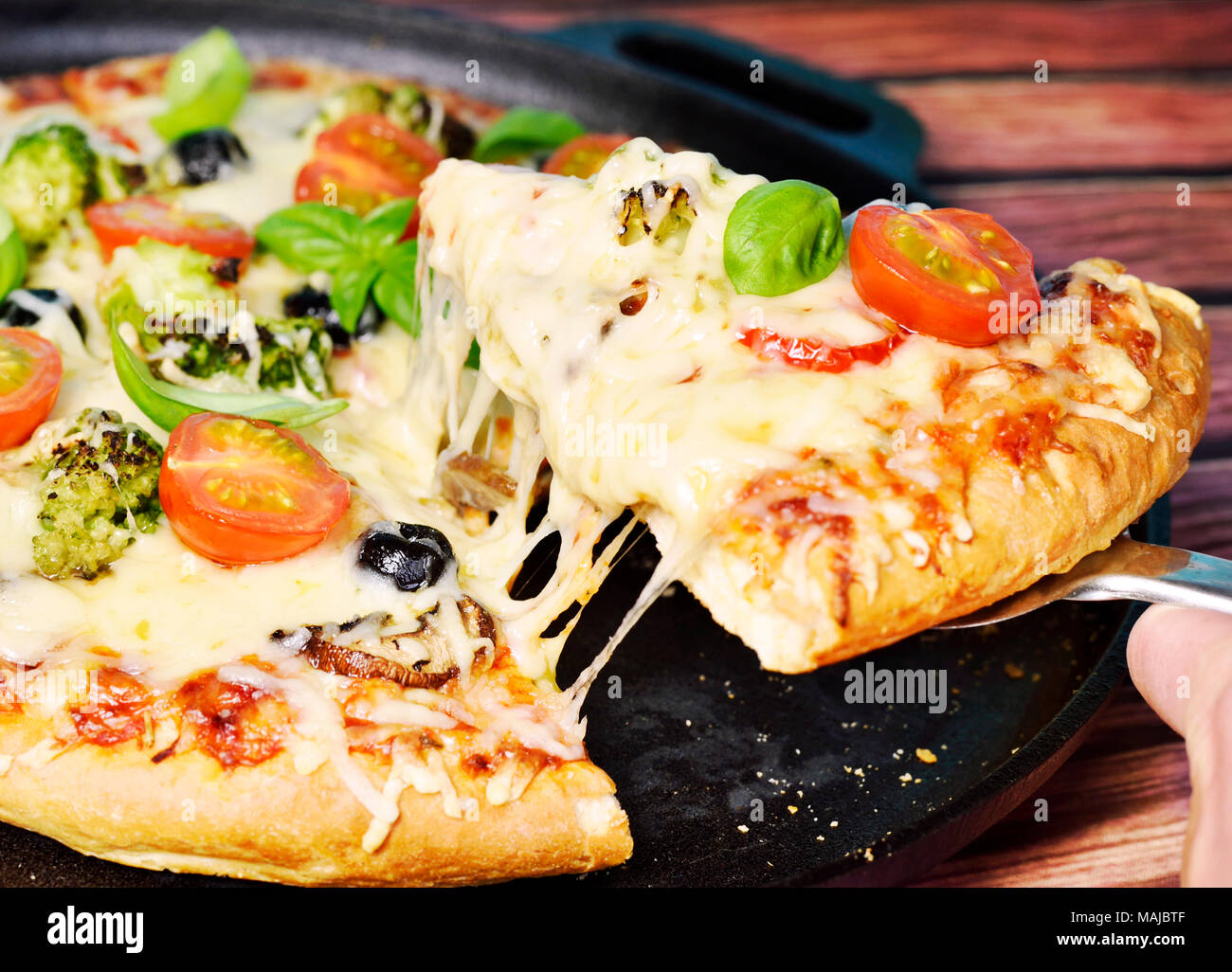 Fresh pizza in a pizza pan. Vegetarian pizza or vegetable pizza with broccoli, tomatoes, mushrooms, olives and cheese. Cheesy pizza, homemade pizza. Stock Photo