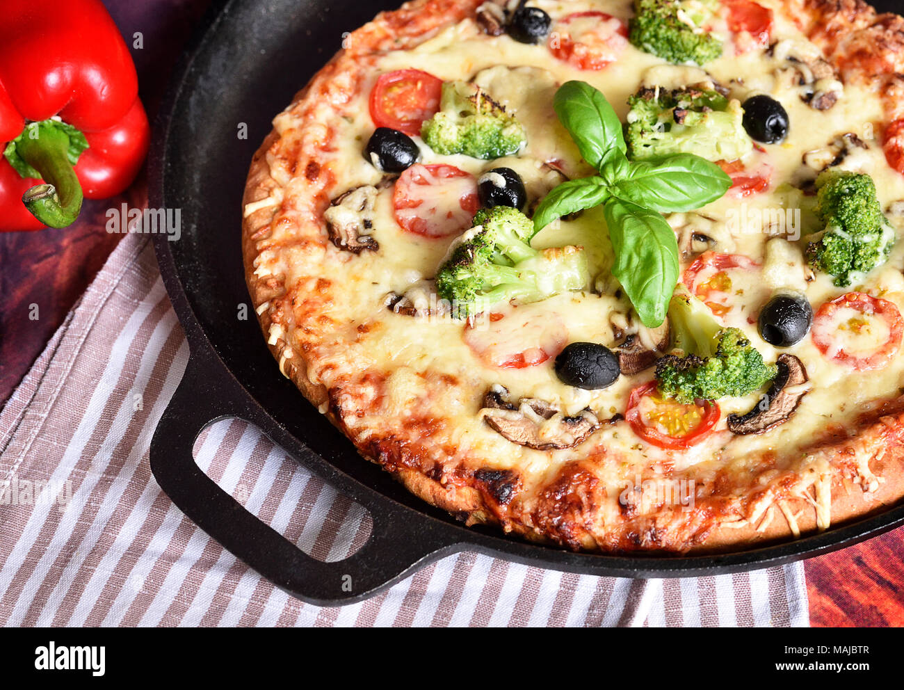 Fresh pizza in a pizza pan. Vegetarian pizza or vegetable pizza with broccoli, tomatoes, mushrooms, olives and cheese. Cheesy pizza, homemade pizza. Stock Photo