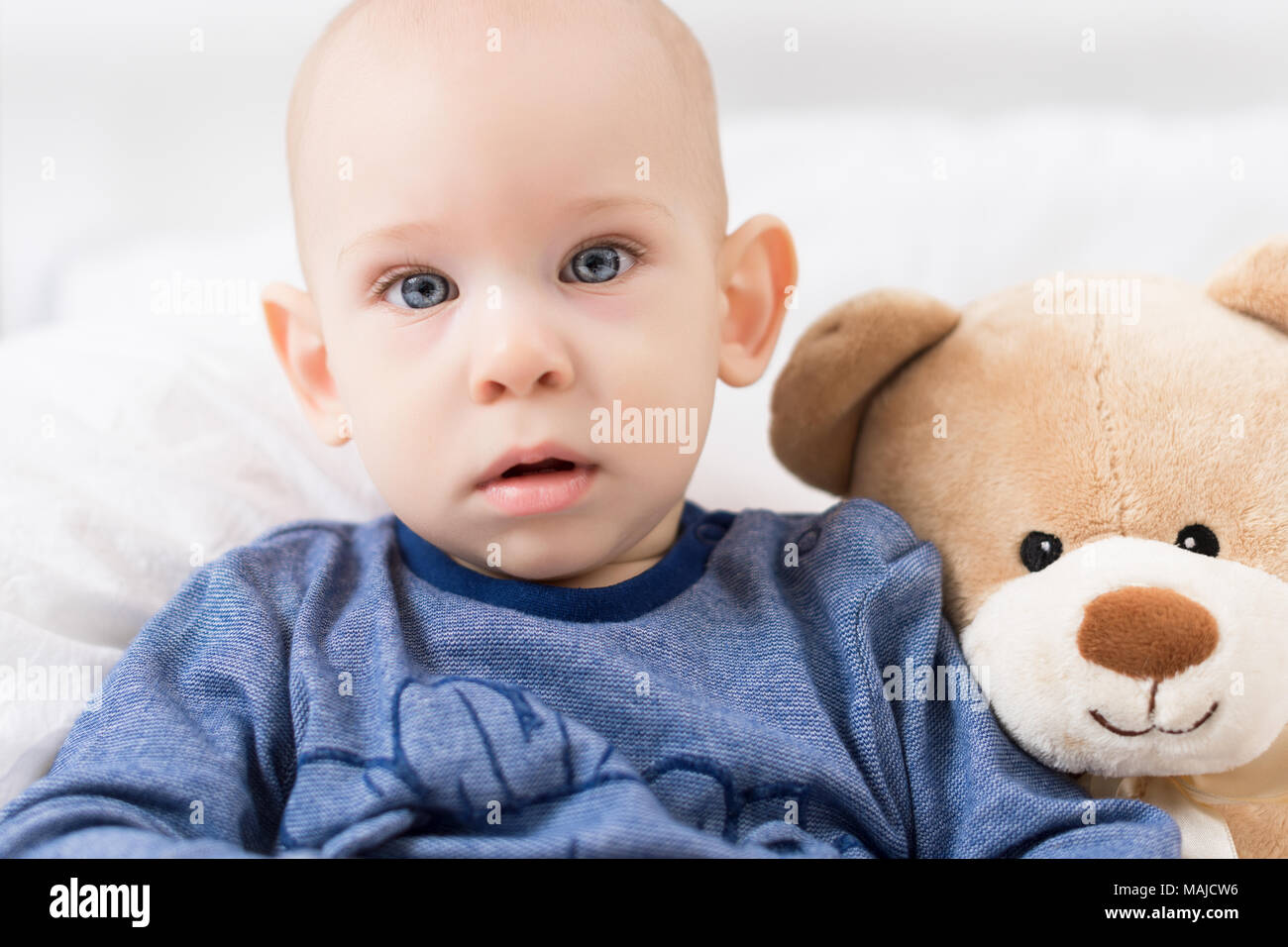 Adorable baby boy sitting on a bed, playing with toy bears on a bed. Newborn child relaxing on a bed. Family morning at home. Stock Photo