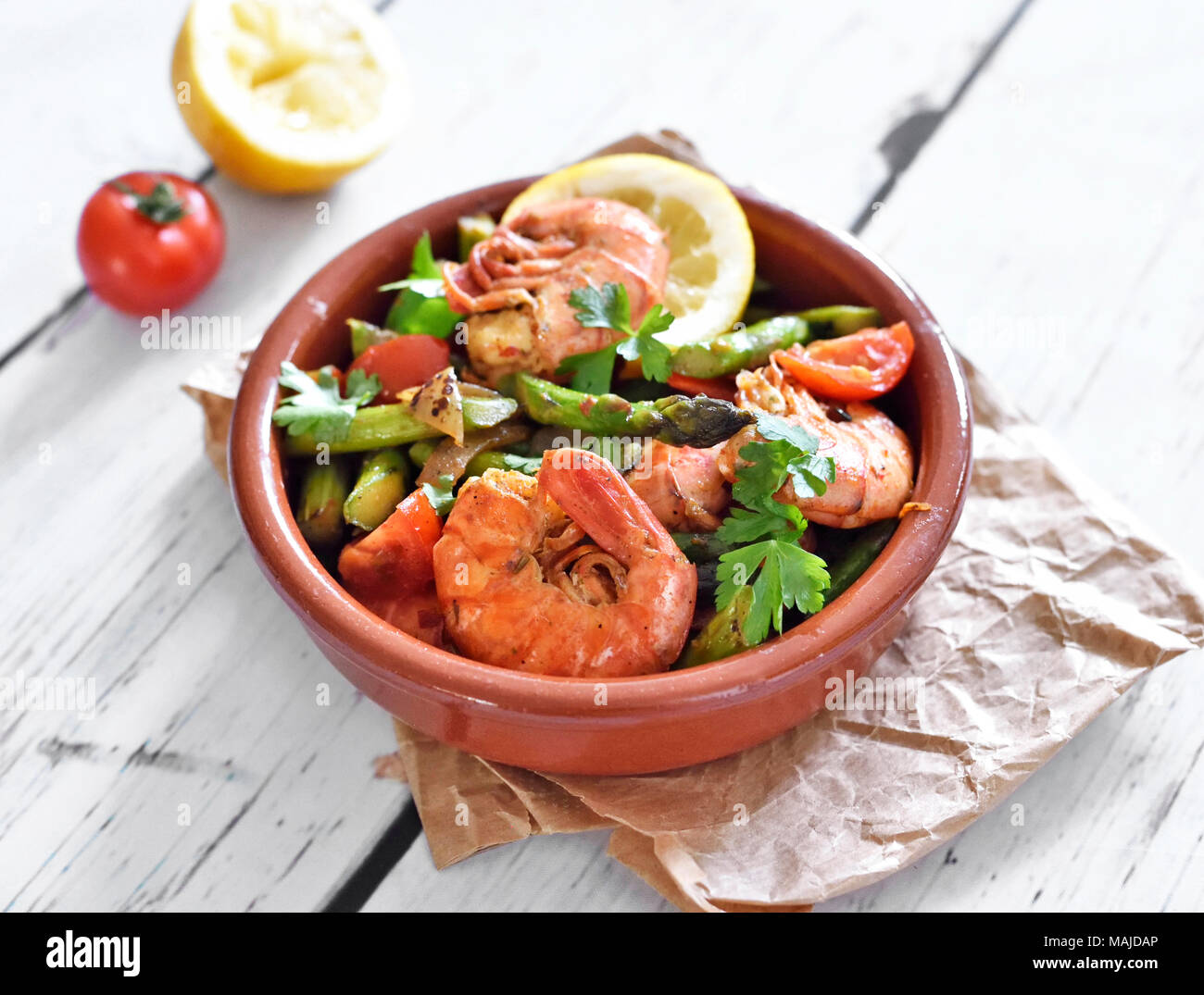 Fresh tapas plate with shrimps and green asparagus, lemon slice and parsley. Gourmet dish on a white wooden table. Stock Photo