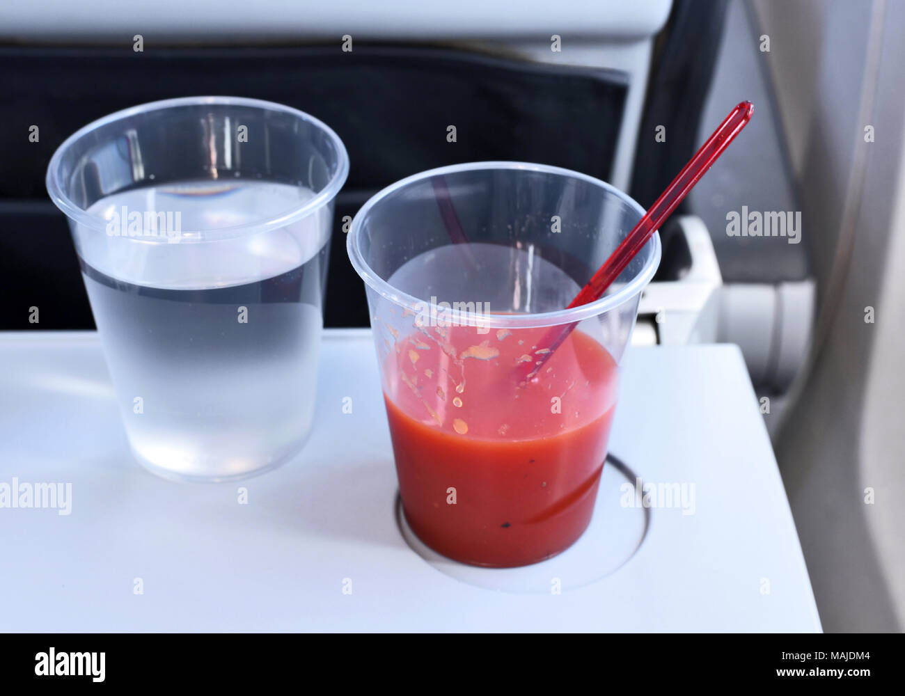 Travel by plane, flight service. Two drinks on an airplane seat table. Plastic drinking glasses with water and tomato juice. Stock Photo