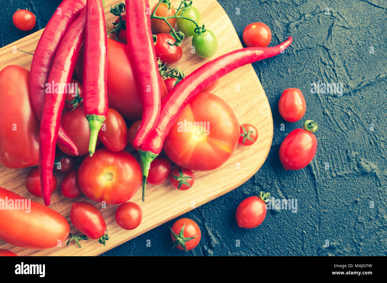 Various colorful tomatoes and red hot chili peppers on wooden board on ...