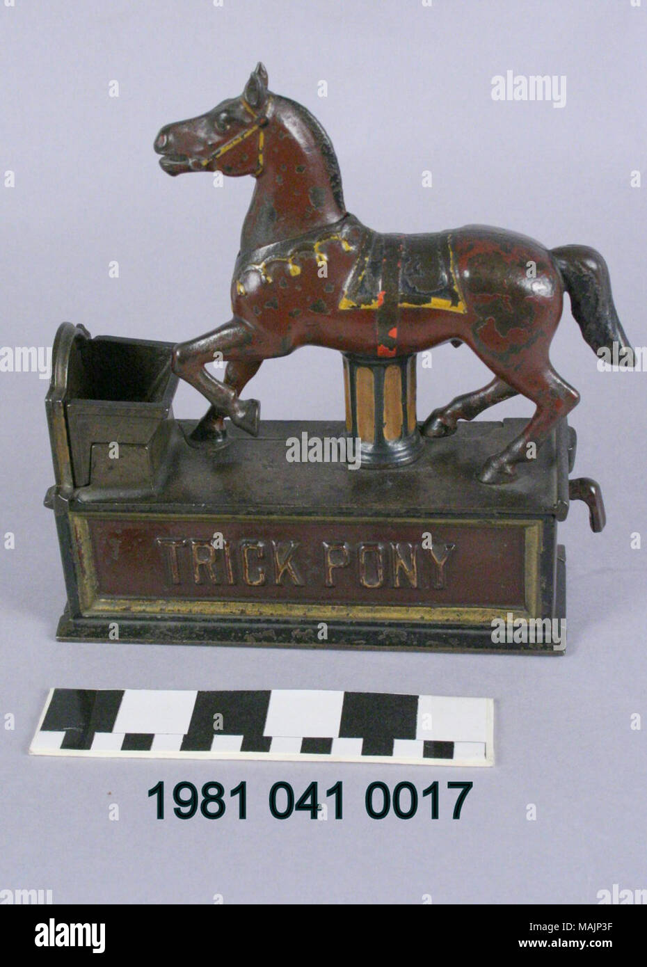 Cast iron mechanical bank in the shape of a horse near a trough. To operate the bank, a coin is placed in the horse's mouth. Pulling a lever on the side of the bank causes the trough floor to open and lowers the horse's head, allowing the coin to fall through the trough into the bank. Manufactured by the Shepard Hardware Company circa 1885. Title: Trick Pony Mechanical Coin Bank  . circa 1885. Peter Adams, Jr. (Designer), Charles G. Shepard (Designer), Shepard Hardware Company (Maker), Stock Photo