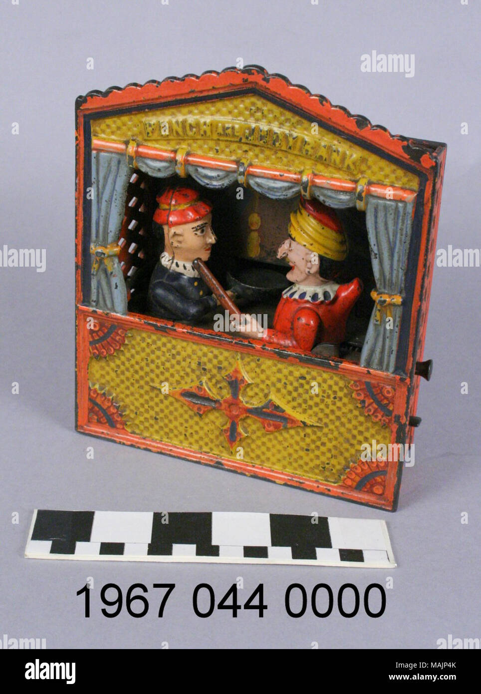 Cast iron mechanical bank depicting a Punch and Judy puppet show. The action is controlled by two levers. the first lever locks the characters in place. To make a deposit, a coin is placed on Judy's tray; a second lever causes Judy to deposit the coin while Punch tries to hit her with a club. Manufactured by the Shepard Hardware Company circa 1884. Title: Punch and Judy Mechanical Coin Bank  . circa 1884. Peter Adams, Jr. (Designer), Charles G. Shepard (Designer), Shepard Hardware Company (Maker), Stock Photo