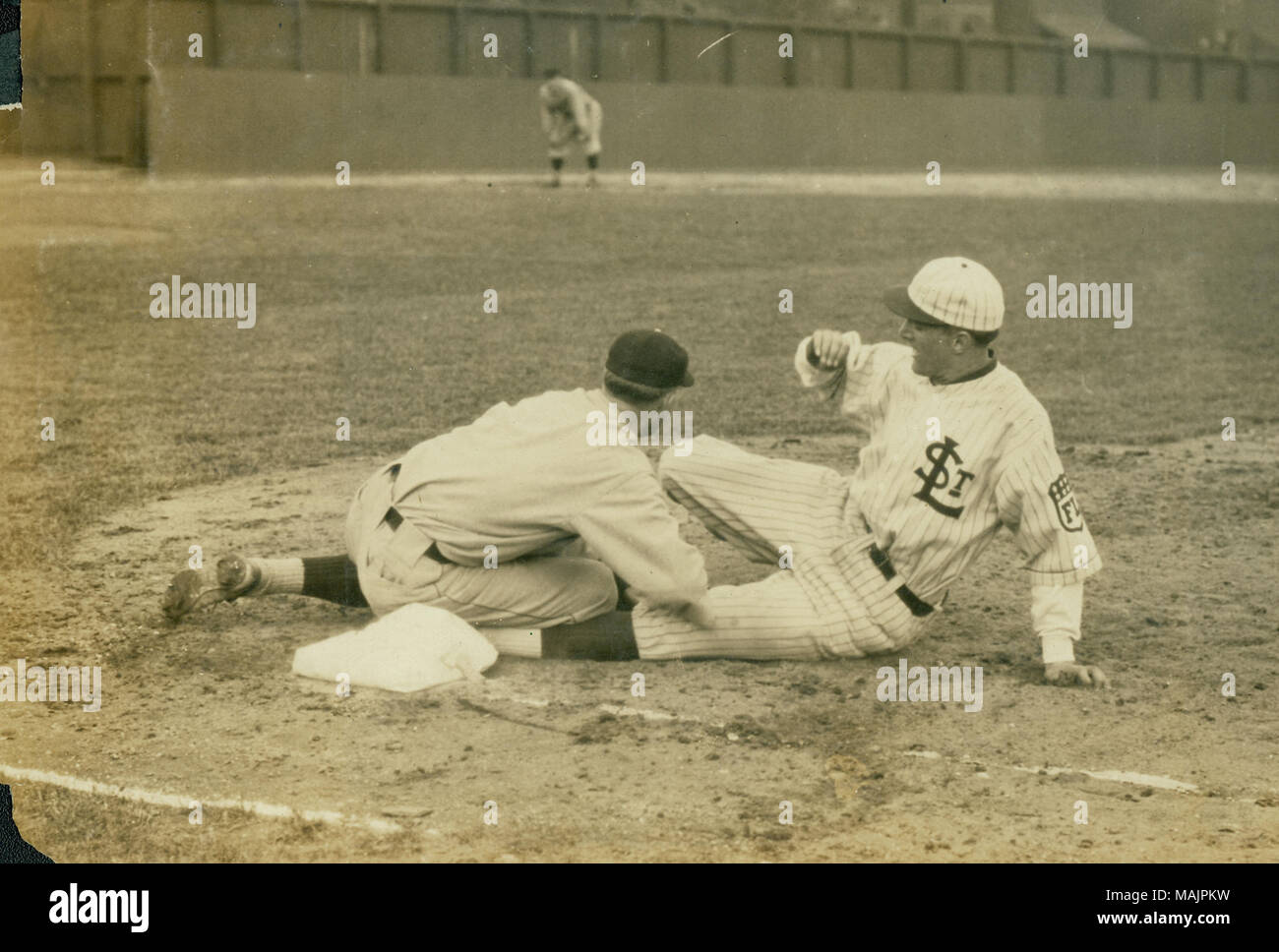 A St. Louis Terriors player is sliding into third base with the third baseman there trying to tag him out. Can also see the center fielder. Title: A member of the St. Louis Terriers baseball team (Federal League) slides into third base during a game.  . between 1914 and 1915. Russell Froelich Stock Photo