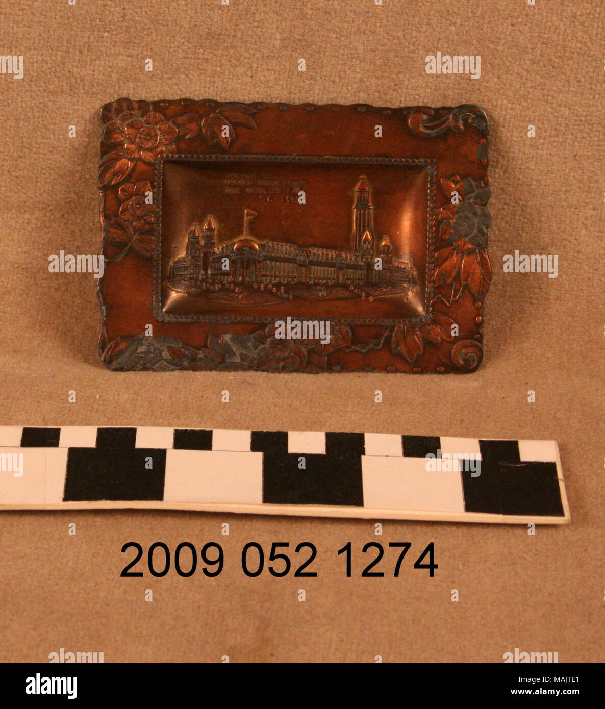 Rectangular copper colored pin tray has relief decoration around outer edge and relief image of the Palace of Varied Industries from the 1904 World's Fair. Title: Metal Pin Tray With Relief Image of the Palace of Varied Industries  . 1904. Stock Photo