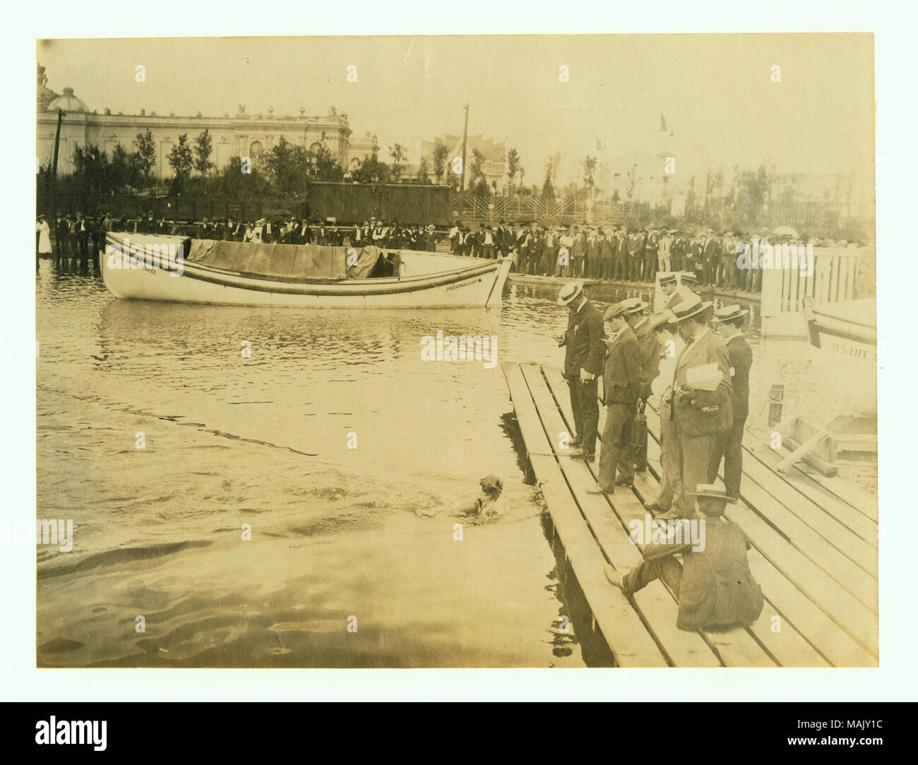 Horizontal photograph of judges standing on a dock looking at a swimmer who has reached the dock. A large crowd of spectators stands on the shore. Title: 1904 Olympics: Daniels of the New York Athletic Club winning the 440 yard swim.  . 1904. Stock Photo
