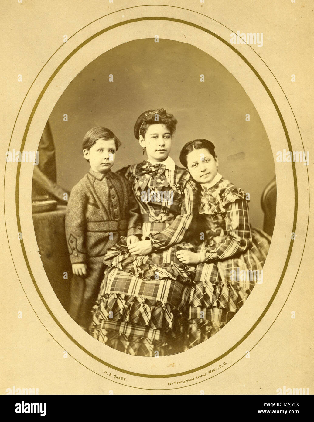 Group portrait of Fannie age 12, Emlie age 14, and Johnson age 5years-8 months. Girls are wearing matching plaid dresses with ruffles and bows and Johnson is wearing a military tailored one piece wool suit with braid and button. Title: Children of Hamilton Fant: Fannie, Emlie and Johnson Fant.  . circa 1860s. Mathew Brady, Washington D.C. Stock Photo