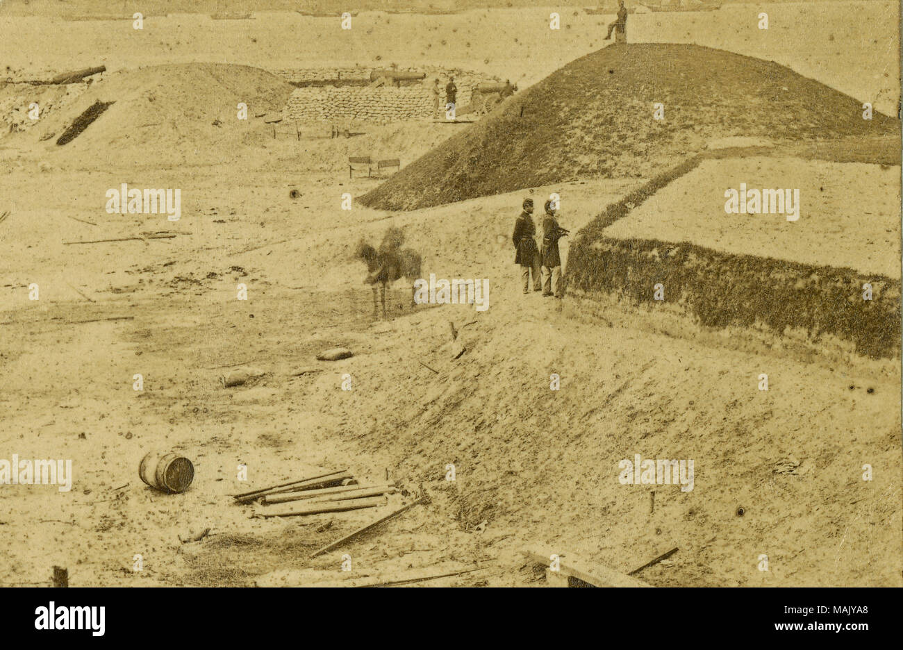 Photograph of earthen bunkers with two officers in the foreground, one rider on a horse, and one man sitting atop one of the bunkers. There are cannons and ships in the background. 'Confederate works Yorktown Va 1862 Gloucester Point in Distance' (written below image). 'Civil War Photo: Confederate works, Yorktown, Va., 1862 Gloucester Point in distance Gift of John H. Gundlach.' (written on reverse side). Title: View of Civil War battlefield at Yorktown, VA.  . 1862. Stock Photo