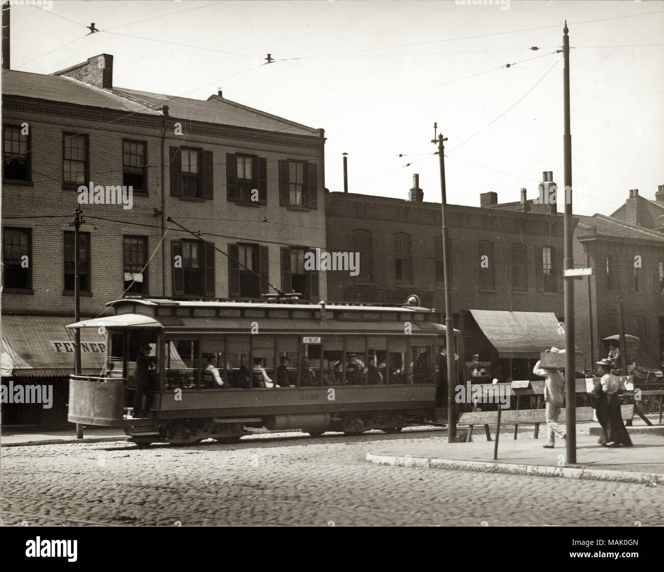 Horizontal, black and white photograph of a trolley filled with passengers moving down a brick paved road. Title: Streetcar at South Tenth and Market Streets.  . circa 1915. Stock Photo
