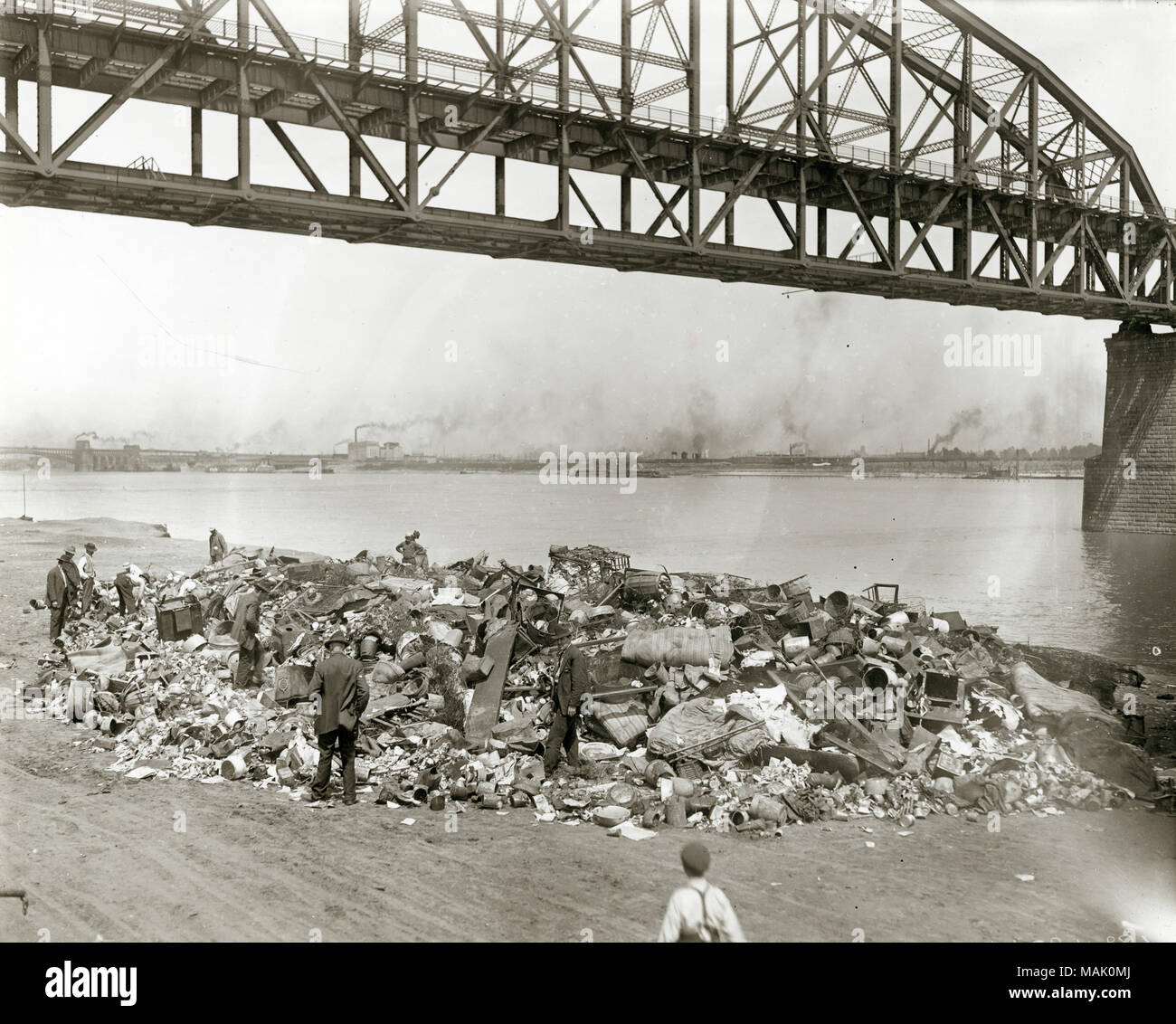Men going through a rubbish pile on the riverfront south of the Municipal Bridge, which was later renamed the MacArthur Bridge. Men going through a rubbish pile on the Mississippi riverfront south of Municipal (MacArthur) Bridge. Started in 1907 and finally opened for automobile traffic in 1917, the Municipal Bridge was built by the city of St. Louis to compete with the monopoly of traffic across the Mississippi River held by the Terminal Railroad Association who owned both the Eads and the Merchants Bridges. The bridge featured an upper deck for automobile traffic and a lower deck for rail ca Stock Photo