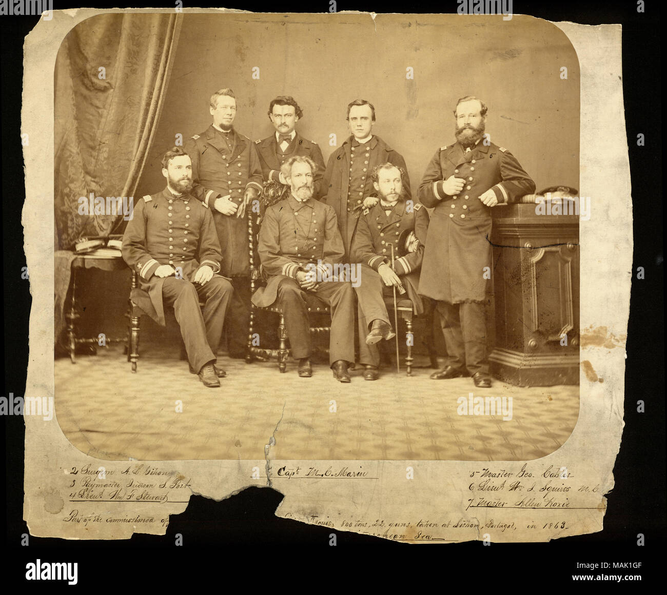 Full-length group portrait of seven men in uniform. The men have numbers written on their images that corrrespond to a handwritten identification below the print. 1. Capt. M. C. Marin; 2. Surgeon A. L. Gihon; 3. Paymaster Judson S. Post; 4. Lieut. Wm. F. Stewart; 5. Master Geo. Cables; 6. Lieut Wm. Squires M. C.; 7. Master Allen Hoxie. A brief caption handwritten below the image reads: 'Part of the commissioned officers of the U.S. Sloop of war Saint Louis, 800 tons, 22 guns, taken at Lisbon, Portugal, in 1863 - while on a 3 years Cruise in the Mediterranean Sea.' A portion of the original cap Stock Photo