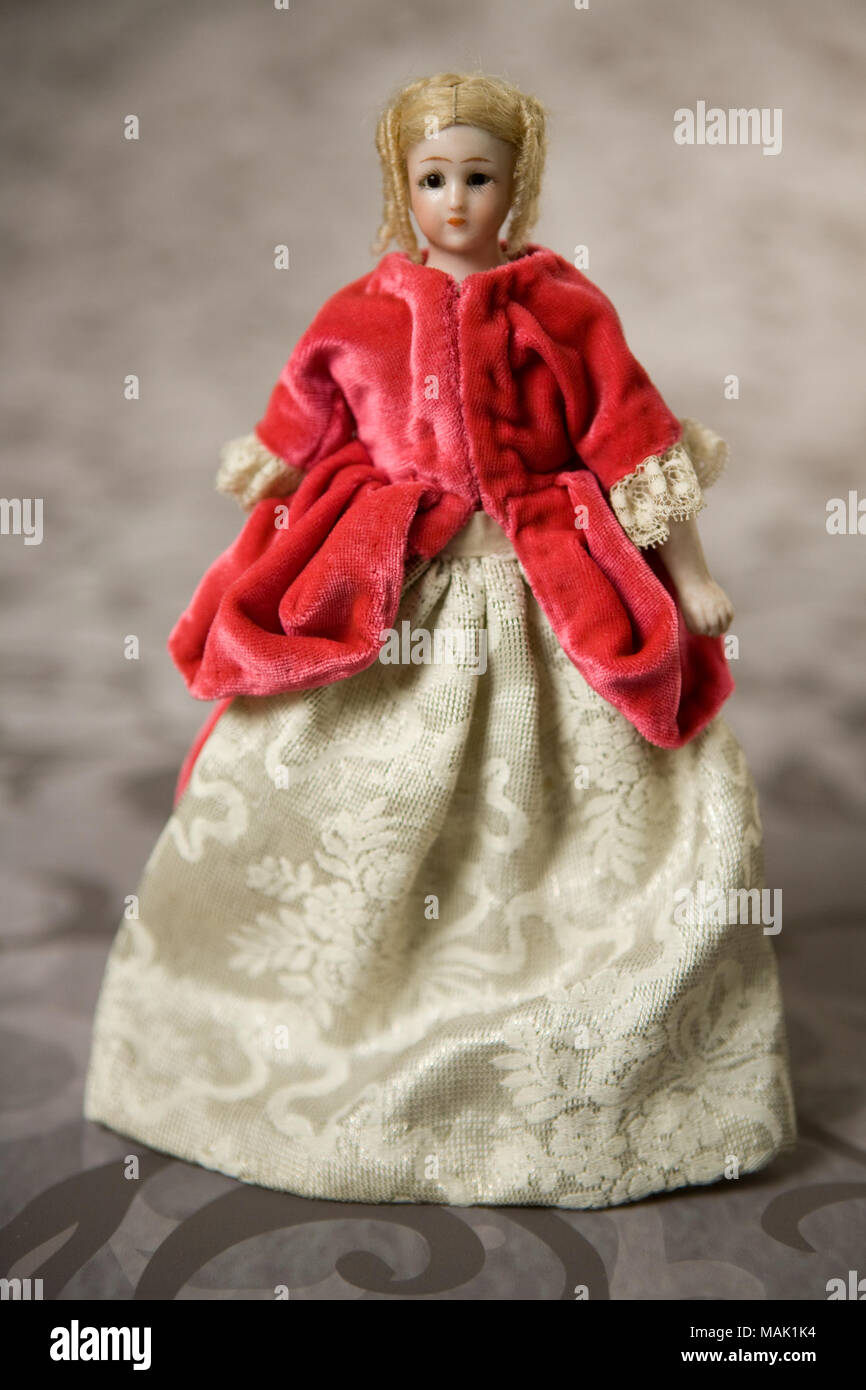 Small bisque head doll has bisque limbs and cloth body. She is wearing a fuschia jacket with a white and silver metallic thread skirt. Title: Simon and Halbig Bisque Doll Wearing Fuschia Velvet Jacket with White and Silver Skirt  . circa 1890. Stock Photo
