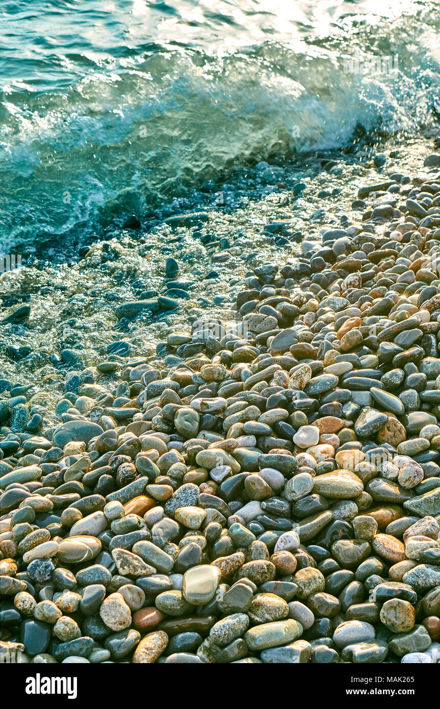 Many colorful stones shinig like a gold under the sun on the beach coastline vertical background with a sunstars Stock Photo