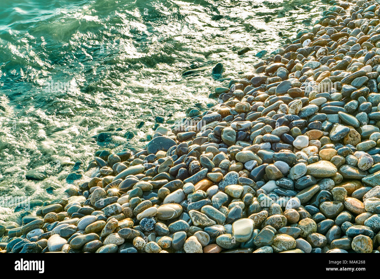 Many colorful stones shinig like a gold under the sun on the beach coastline background with a sunstars Stock Photo