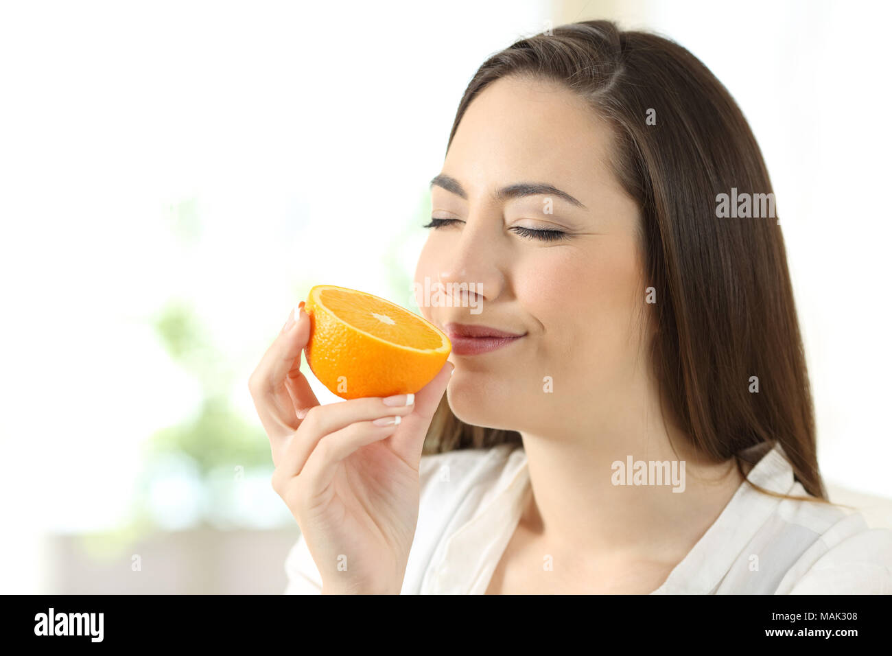 Portrait of a pretty woman smelling half orange at home Stock Photo