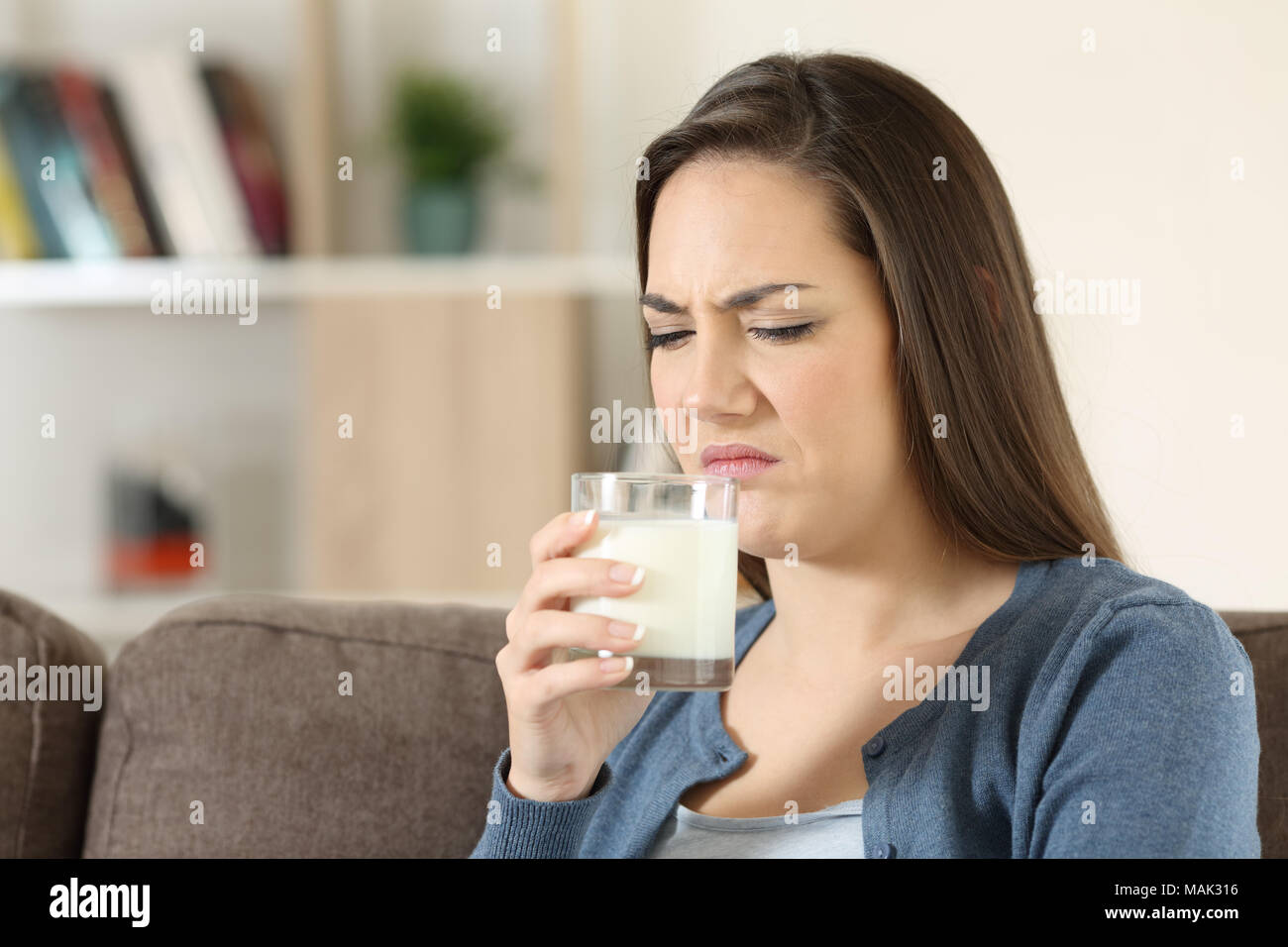 Disgusted woman tasing milk with bad flavor sitting on a couch in the living room at home Stock Photo