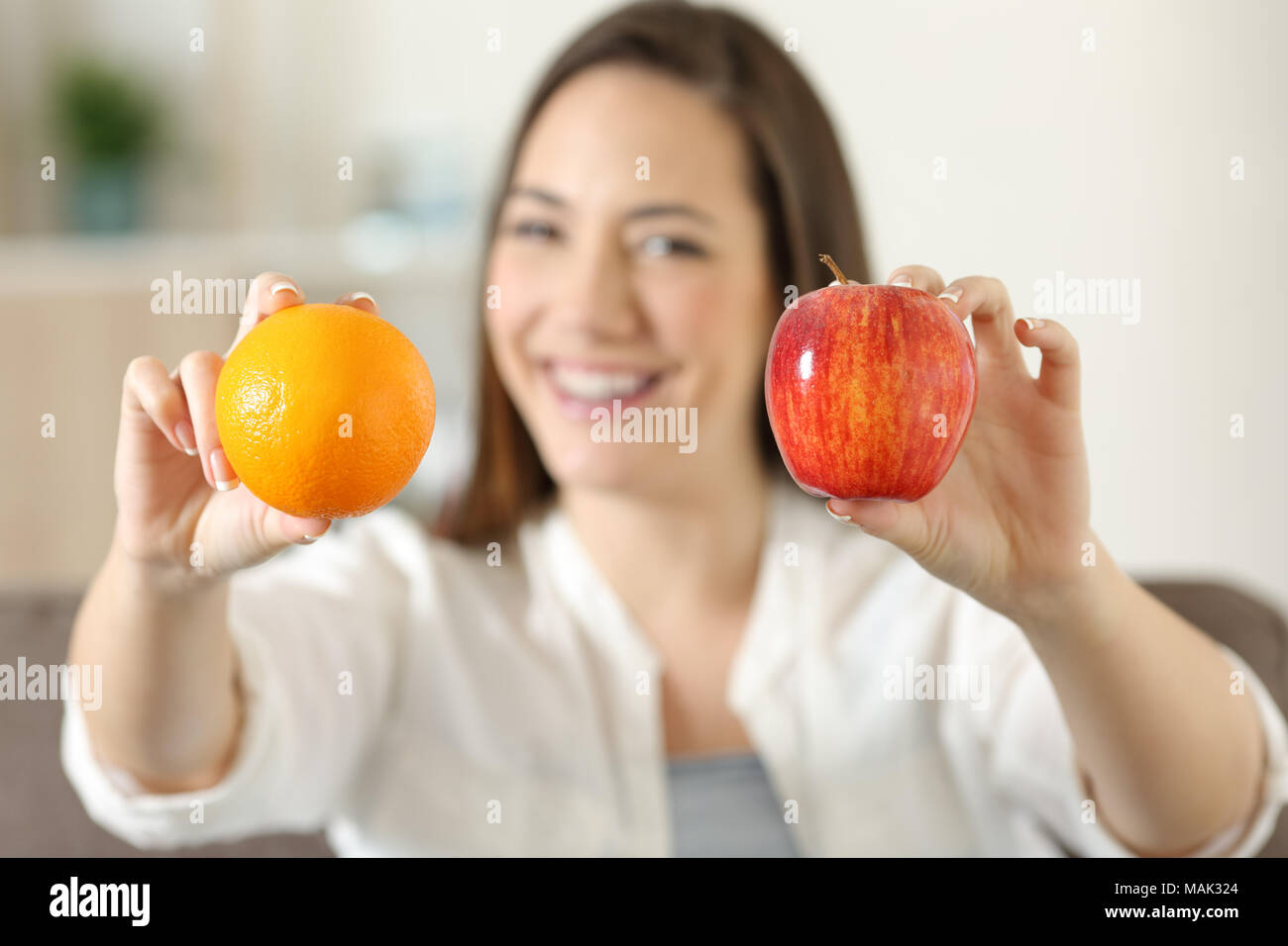 Front view portrait of a happy woman showing two different fruits sitting on a couch in the living room at home Stock Photo