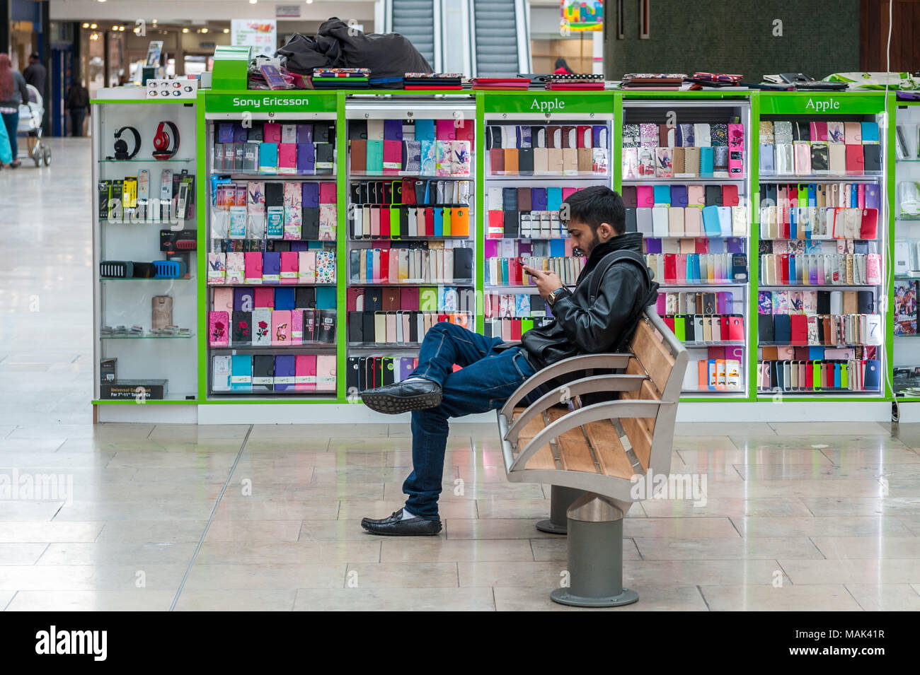 Mobile Phone cover/case stall with man sitting on bench using a mobile phone in Lower Precinct, Coventry, West Midlands, UK. Stock Photo